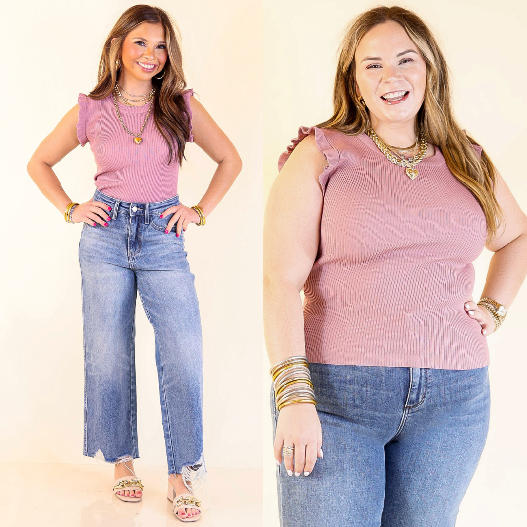 Two women wearing mauve pink ruffle sleeve top and blue jeans on a plain background.