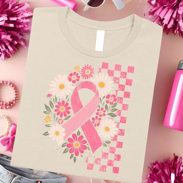 Beige t-shirt with pink ribbon and floral design on a pink background with accessories.