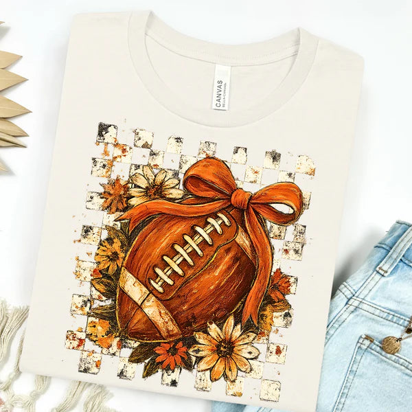 Short sleeve tee with checkered and floral football graphic, topped with a bow, perfect for fall game day or casual wear.