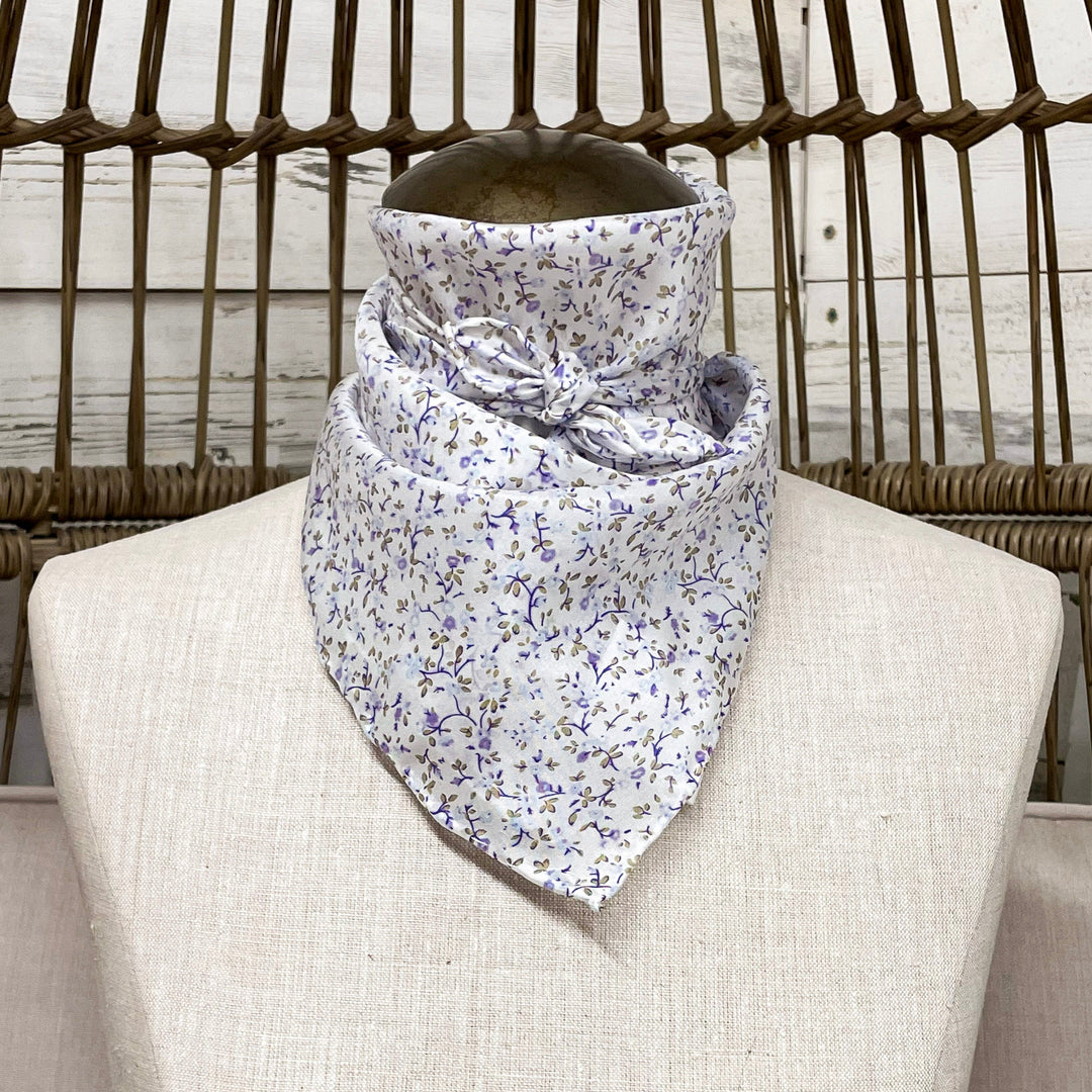 A white wild rag with purple and green floral detailing, tied around a mannequin neck