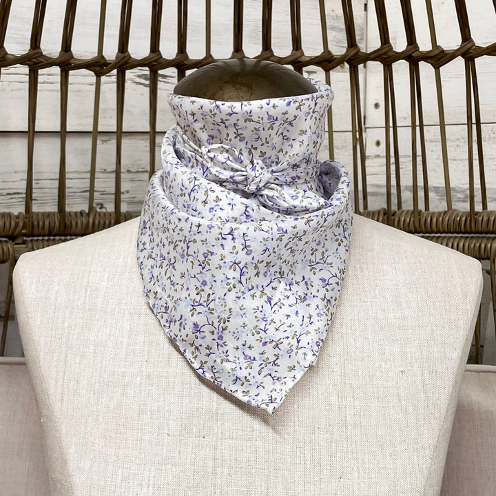 A white wild rag with purple and green floral detailing, tied around a mannequin neck