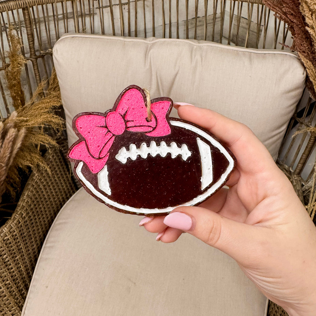 A hand holding a football freshie that has a pink bow in it with a rustic chain background