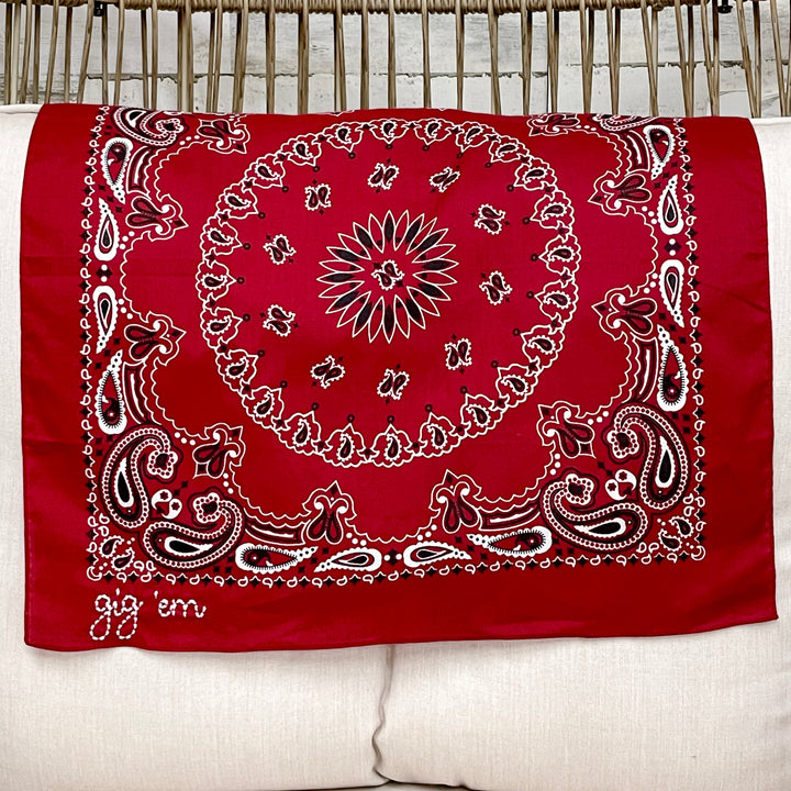 Maroon bandana with white patterns on a white pillow against a white chair background.