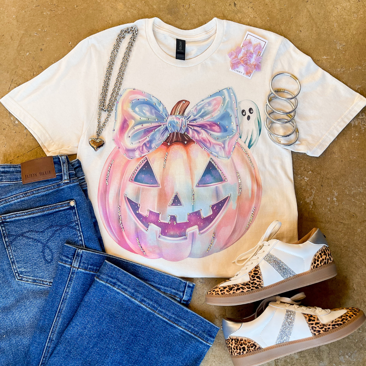 T-shirt with a colorful pumpkin design, jeans, and sneakers on a brown background.