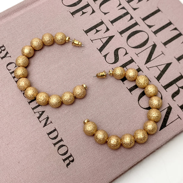 Gold tone beaded medium size hoop earrings. These Earrings are pictured on a white background with part of it on a pink book.