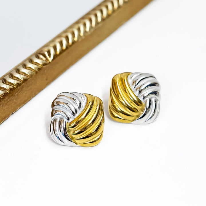 Pair of gold and silver earrings on a white surface with a decorative gold frame.