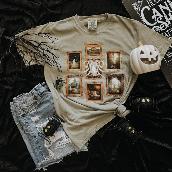 Beige t-shirt with Halloween-themed design, paired with denim shorts and a small pumpkin decoration on a dark background.