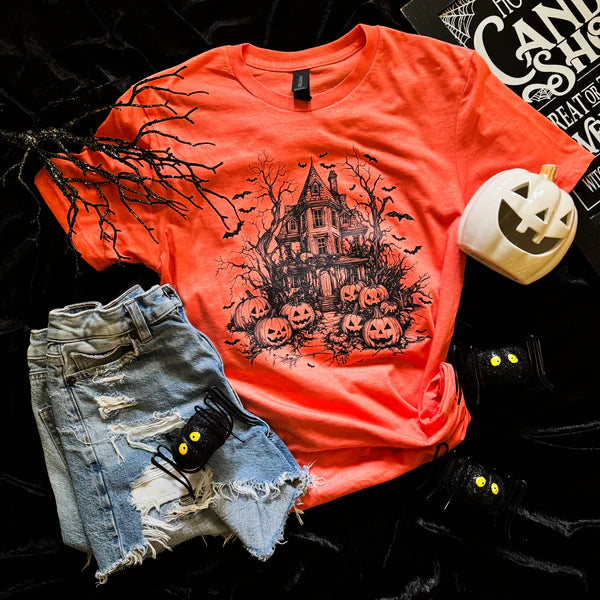 Orange t-shirt with Halloween-themed design, denim shorts, and small pumpkin decoration on a dark background.