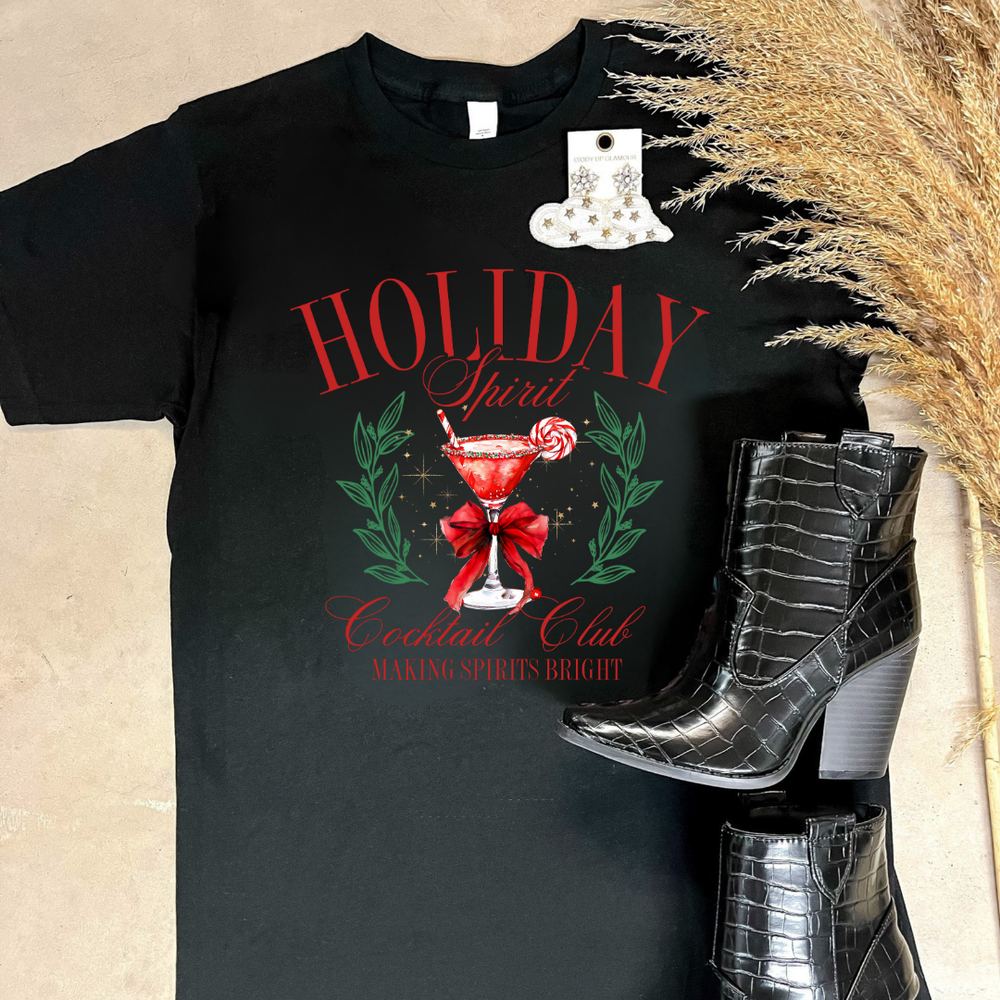 Black tee laid flat with boots, printed with 'HOLIDAY Spirit Cocktail Club' and a peppermint martini.