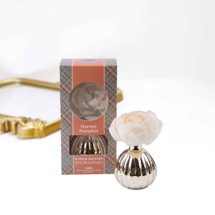 A solid white background with a gold mirror. Upfront is a packaged and unpackaged flower diffuser in the scent harvest pumpkin by bridgewater candle company.