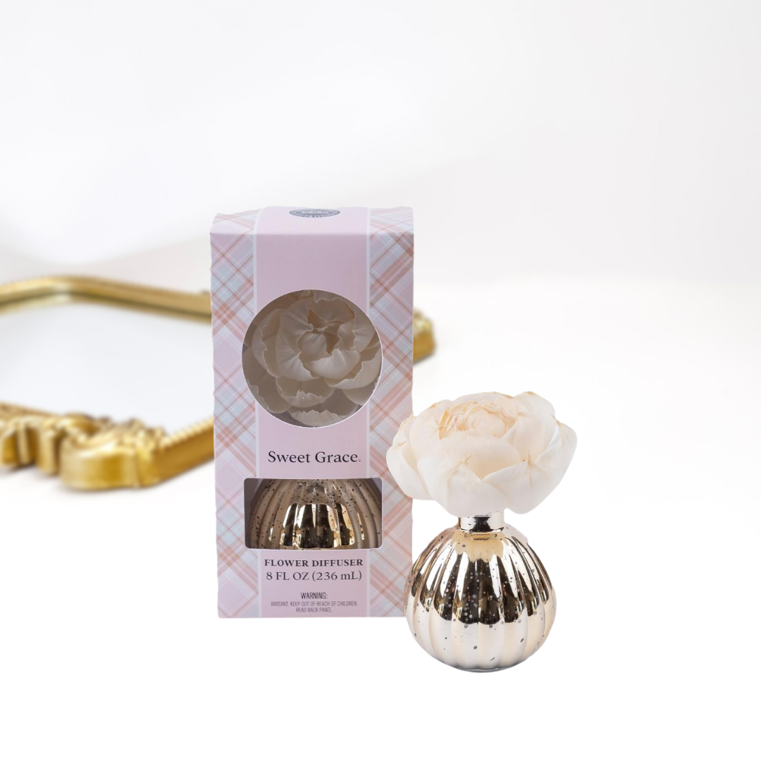 A solid white background with a gold mirror. Upfront is a packaged and unpackaged flower diffuser in the scent sweet grace by bridgewater candle company.