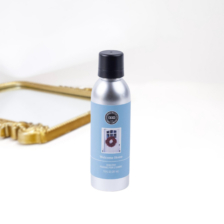 A solid white background with a gold mirror and a bottle of room spray in a silver and black container. Created by bridgewater.