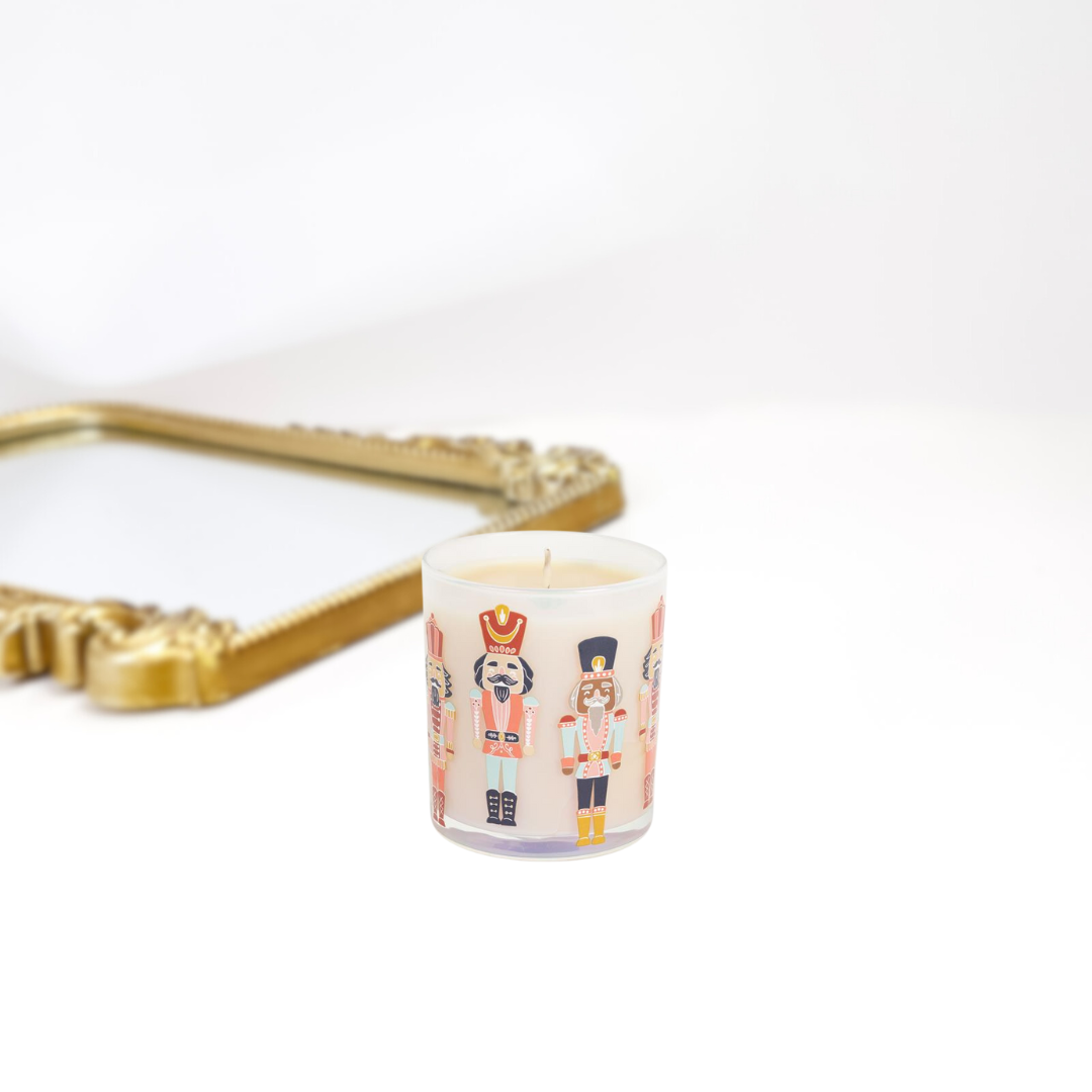A gold mirror on a solid white background. A clear candle with all types of different nutcrackers on it. Perfect for the holiday season.