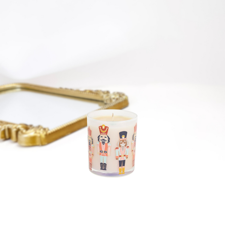 A gold mirror on a solid white background. A clear candle with all types of different nutcrackers on it. Perfect for the holiday season.