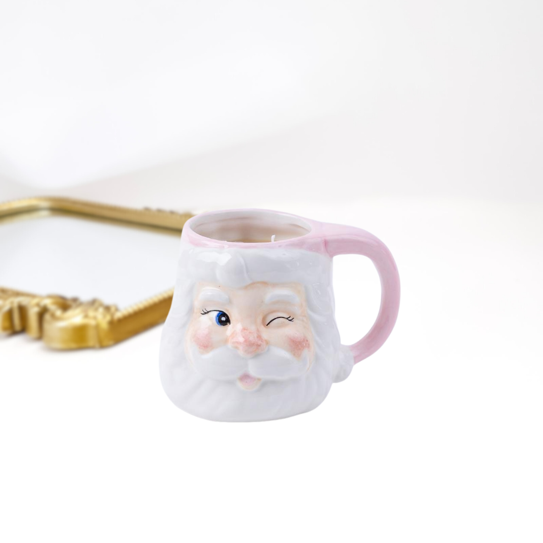 A gold mirror on a white background and a holiday santa mug candle in light pink.