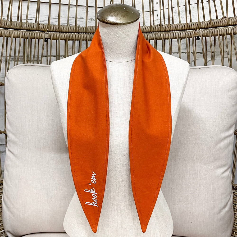 Mannequin wearing an orange scarf with a brand "hook'em" on a wicker chair.