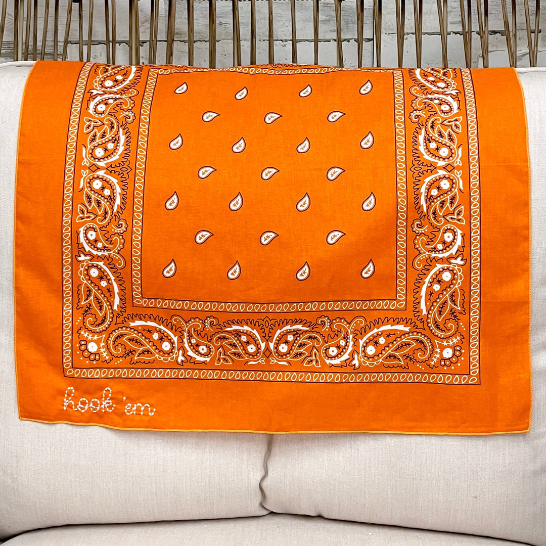 Orange bandana with white patterns on a white pillow in a chair.