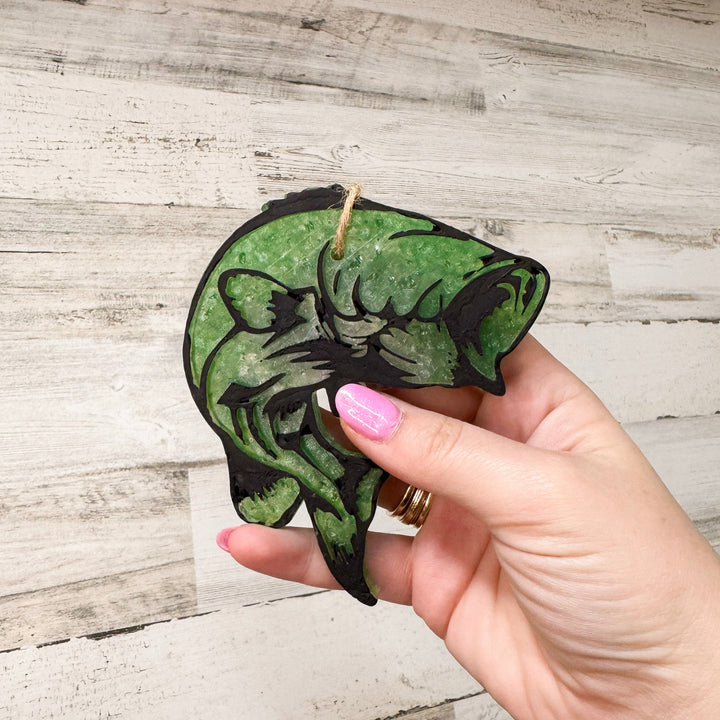 A wooden background with a green fish wax car freshie.