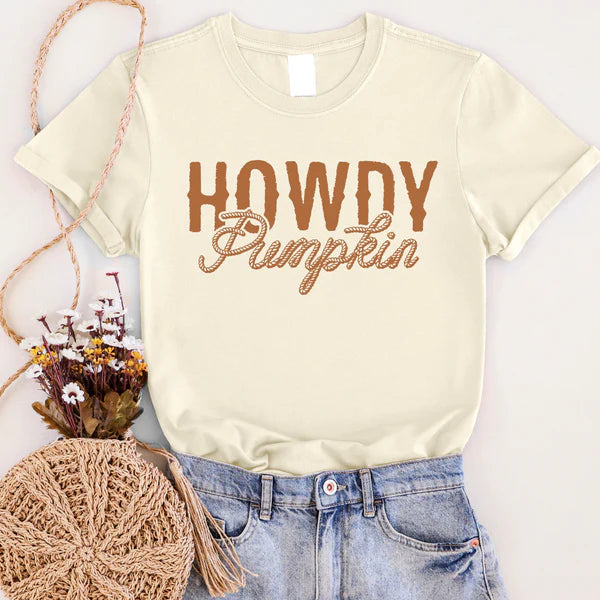 Beige t-shirt with 'Howdy Pumpkin' text, paired with jeans and a woven bag on a light background