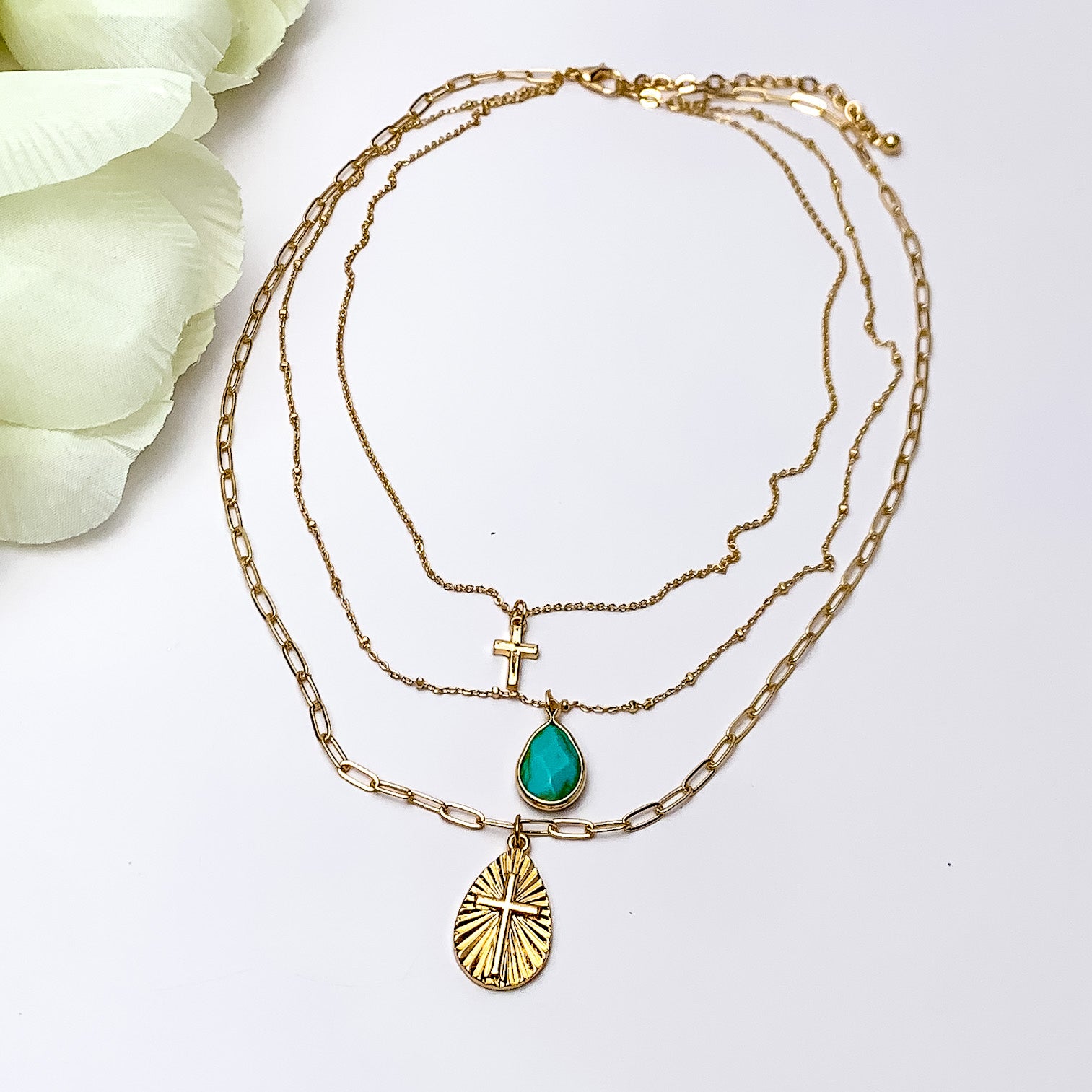 Three layered Gold Tone Necklace With Multiple Designed Charms. Pictured on a white background with a piece of wood behind the necklace.