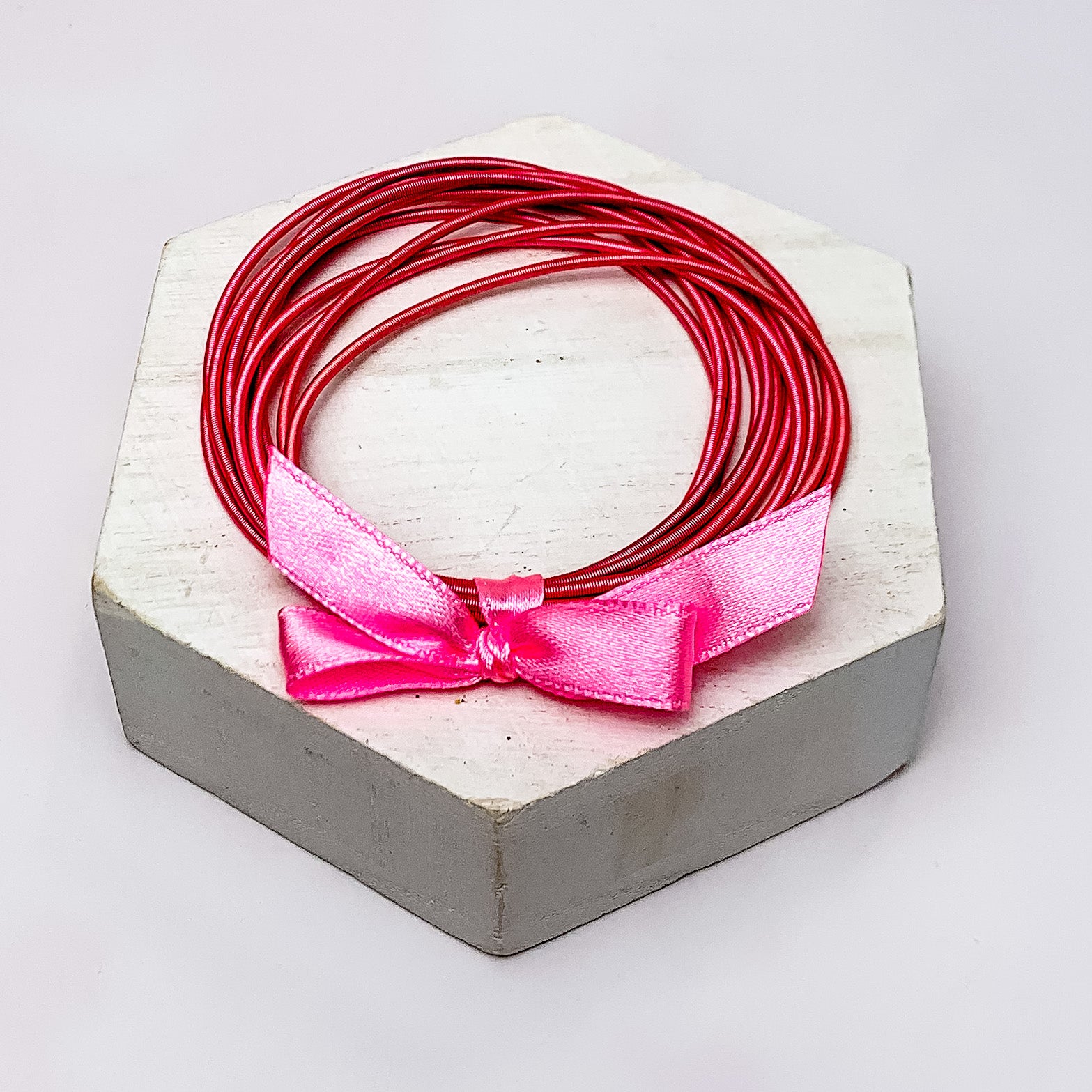 Guitar String Bracelets with Bow in Dark Pink. Pictured on a white background sitting on top of a white block.