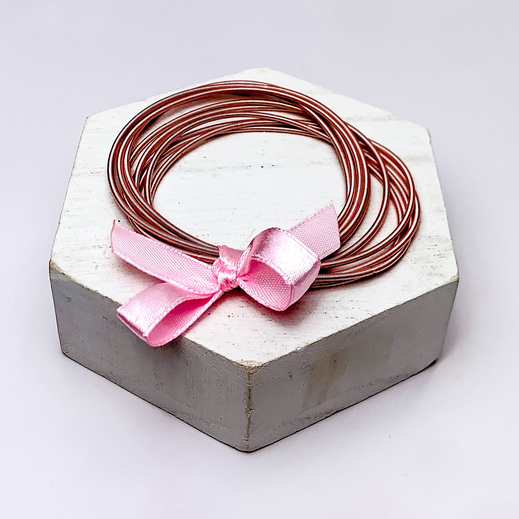 Guitar String Bracelets with Bow in Light Pink. Pictured on a white background sitting on top of a white block.