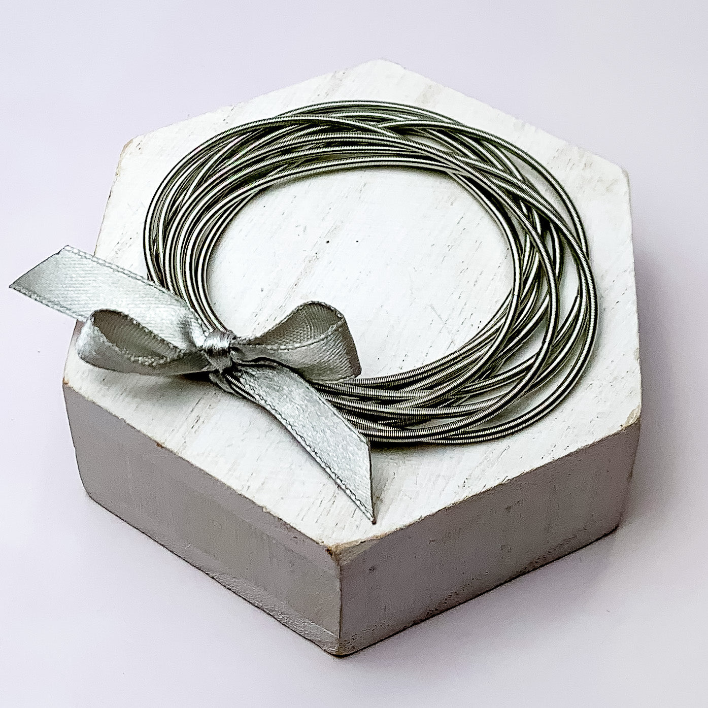 Guitar String Bracelets with Bow in Grey. Pictured on a white background sitting on top of a white block.
