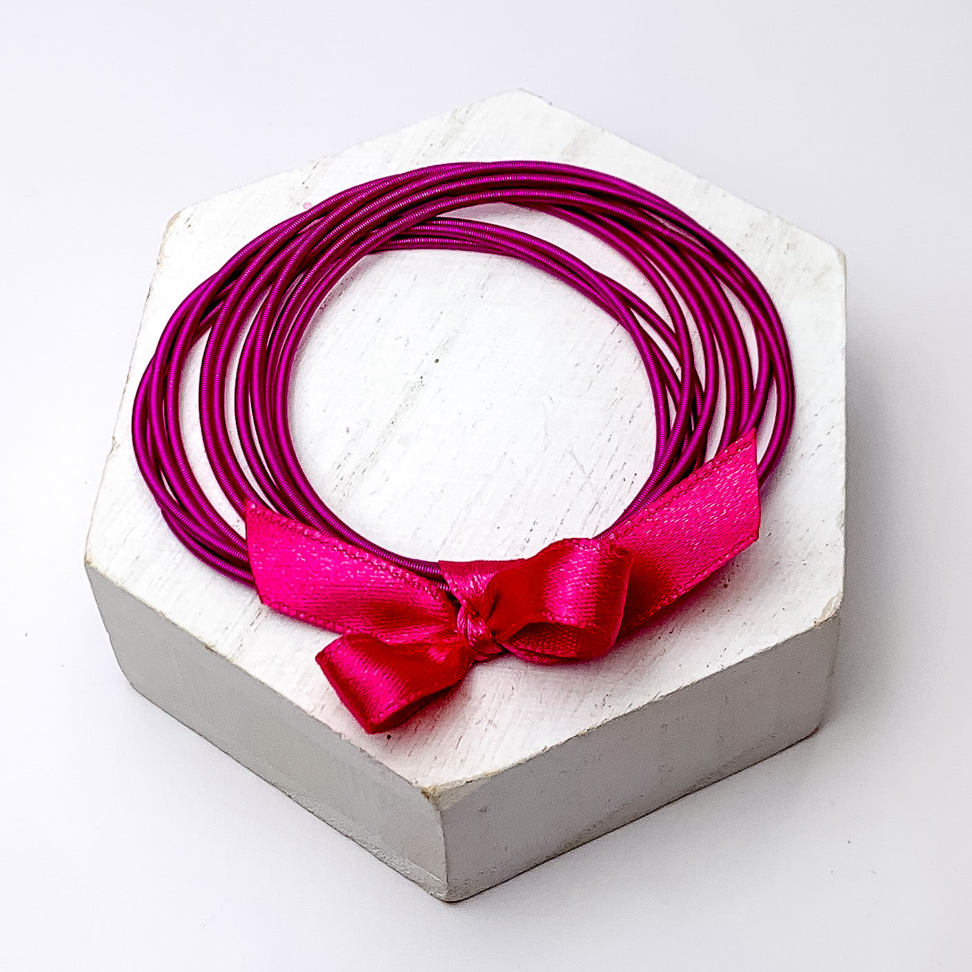 Guitar String Bracelets with Bow in Fuchsia. Pictured on a white background sitting on top of a white block.