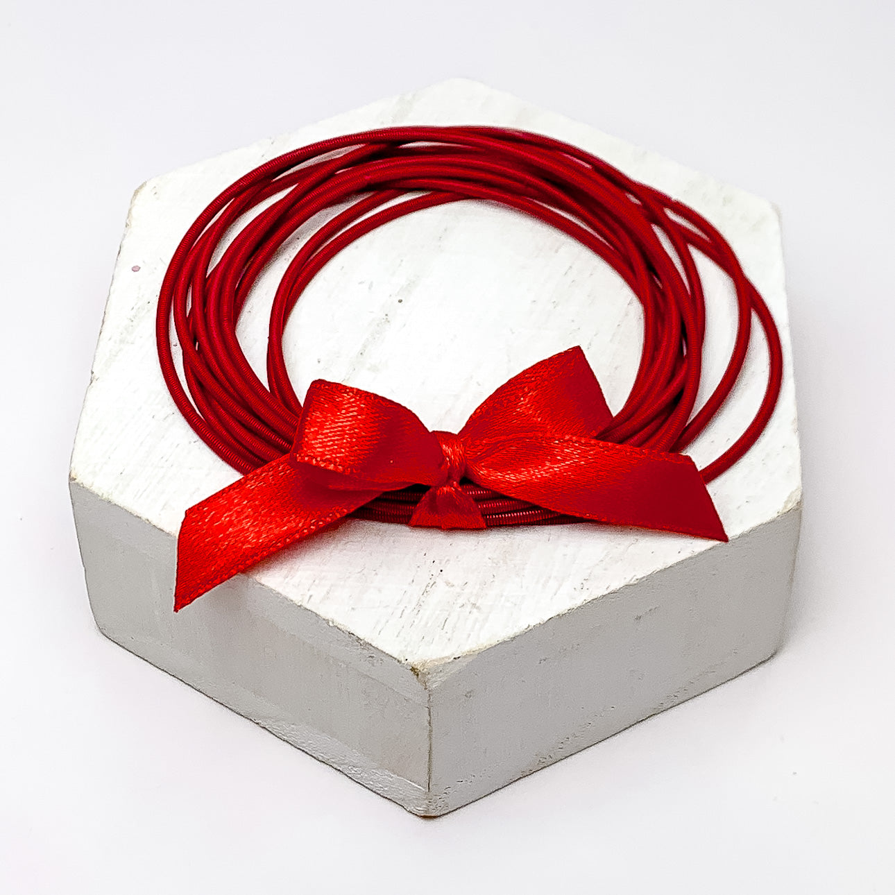 Guitar String Bracelets with Bow in Red. Pictured on a white background sitting on top of a white block.