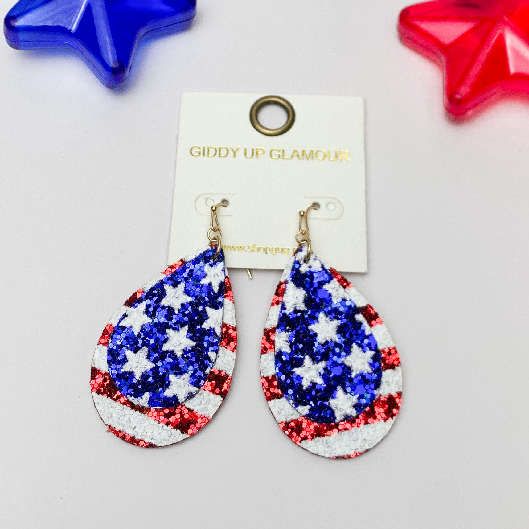 Stars And Stripes Glitter Patriotic Teardrop Earrings. Pictured on a white background with a red and star at the top for decoration.