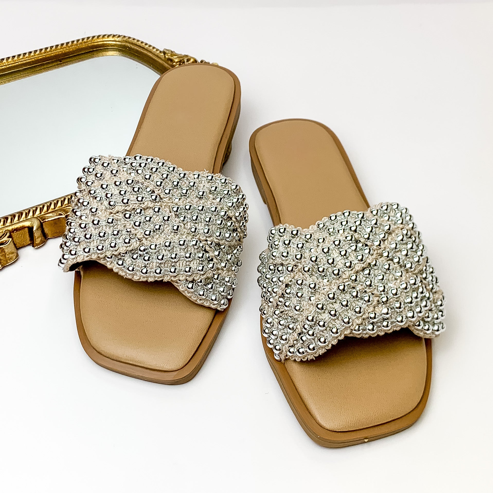 Tan sandals with a nude, knit band that has a silver beaded design. These sandals are pictured on a white background with a gold mirror in the top left corner. 