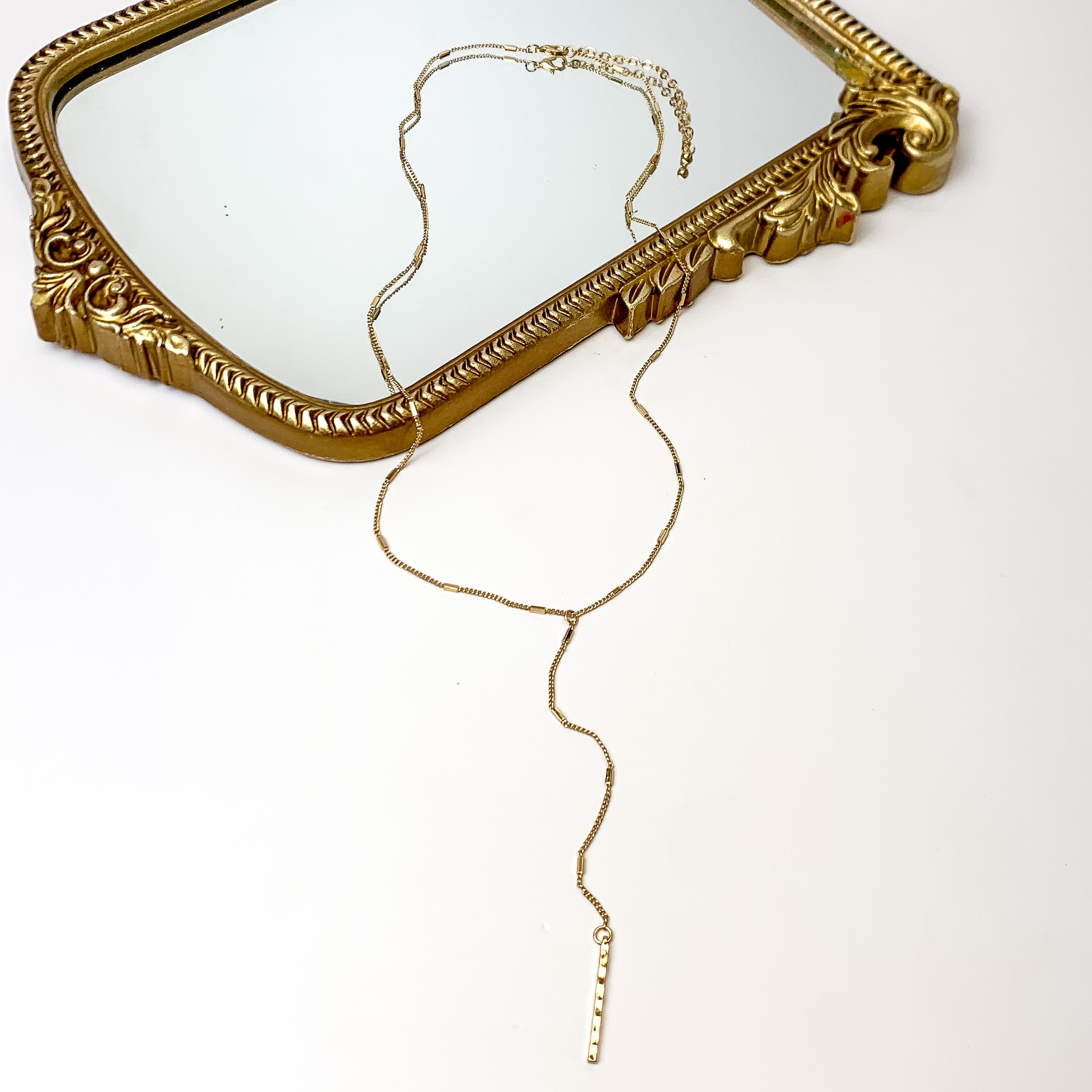 Gold Tone Y Necklace With Hammered Rectangle Charms. Pictured on a white background with the necklace laying on a mirror.