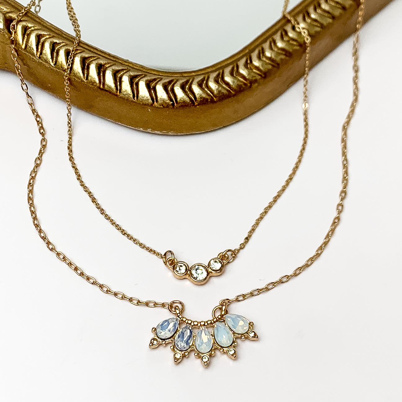 Dazzling Gold Tone Necklace With White Opal Crystals. Pictured on a white background with a gold frame behind the necklace.