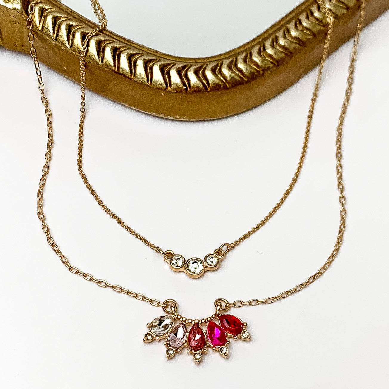 Dazzling Gold Tone Necklace With Pink Crystals. Pictured on a white background with a gold frame behind the necklace.