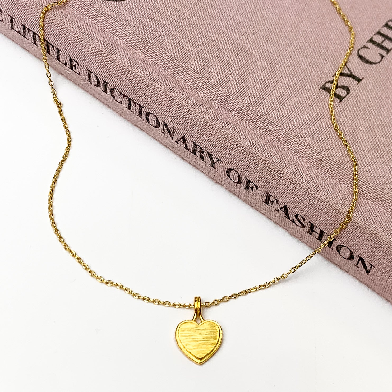 Gold Tone Necklace With Heart Charm. Pictured on a white background with the necklace laying on a book.