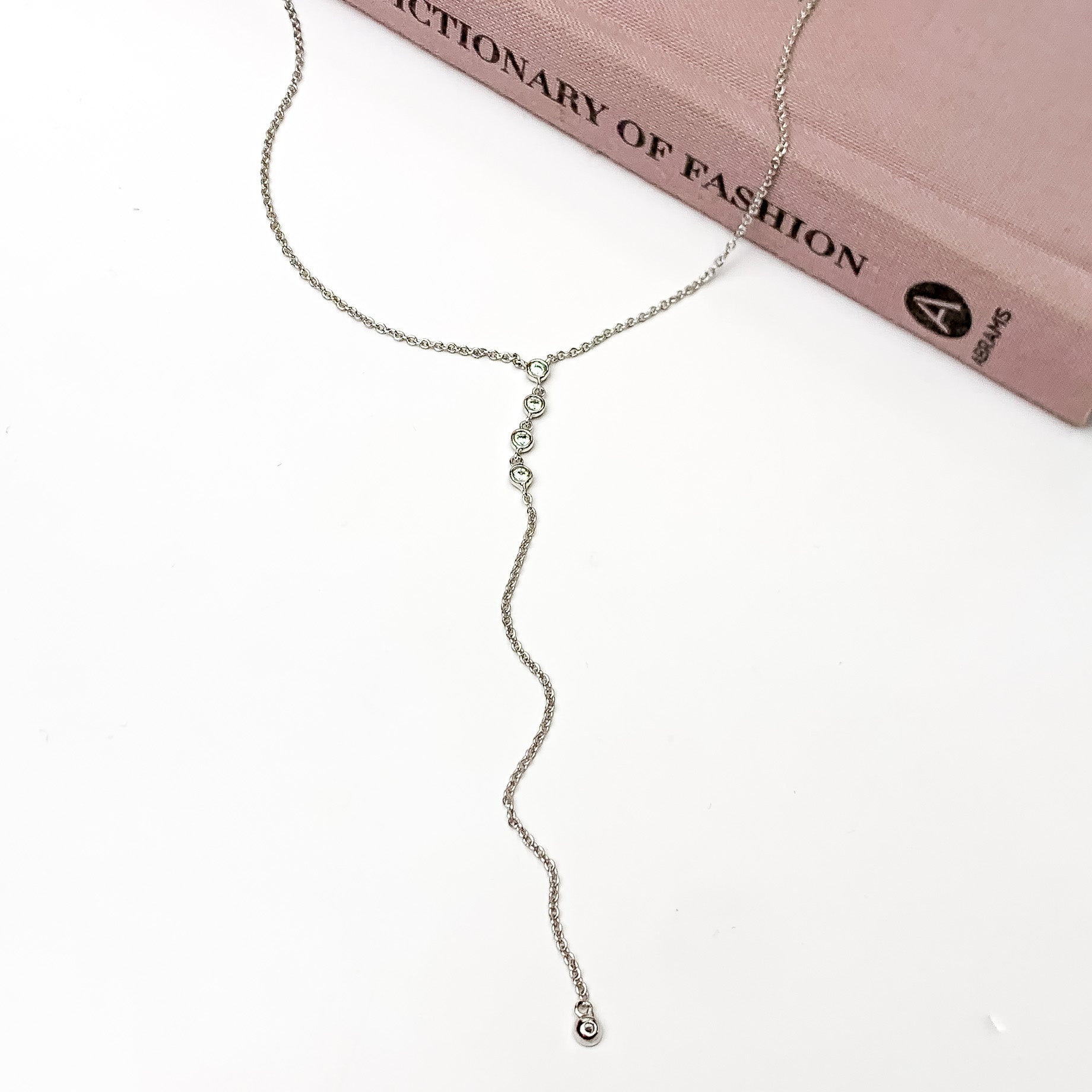 Silver Tone Y necklace With Clear Crystal Accessory. Pictured on a white background with the necklace laying on a closed book.