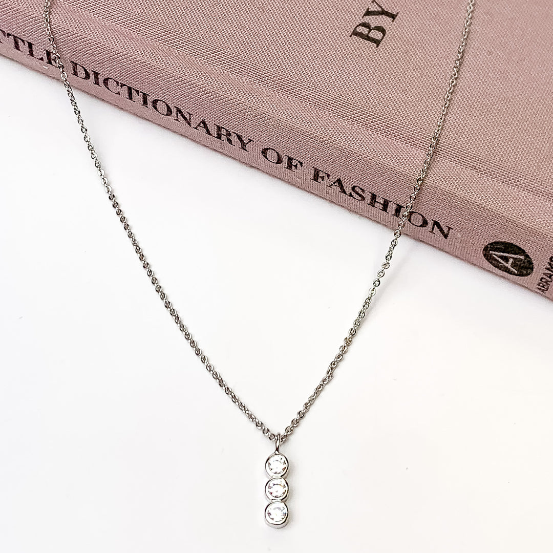 Triple Clear Crystals Silver Tone Necklace. Pictured on a white background with the necklace laying on a book.