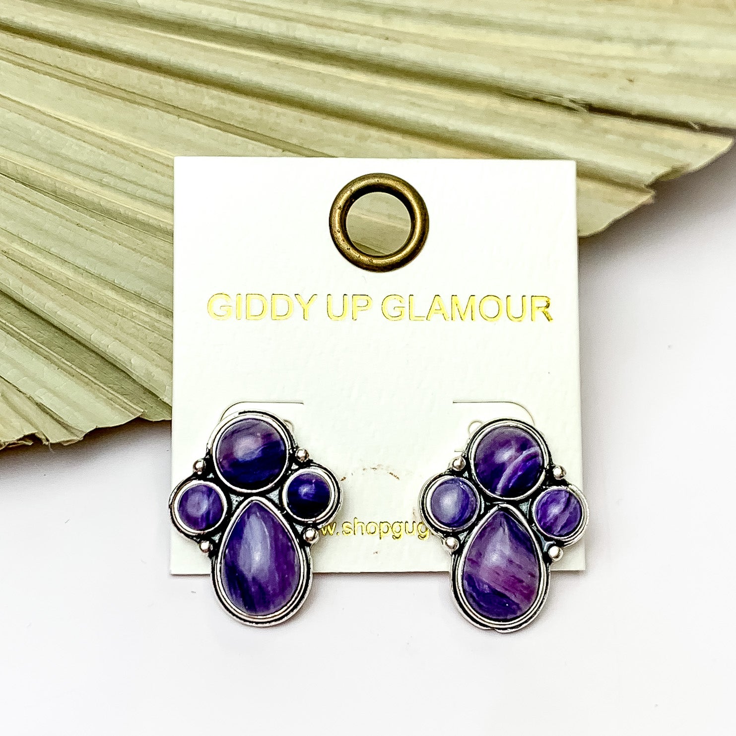 Silver Tone Cluster Stone Earrings in Purple. Pictured on a white background with a leaf fan behind the earrings.