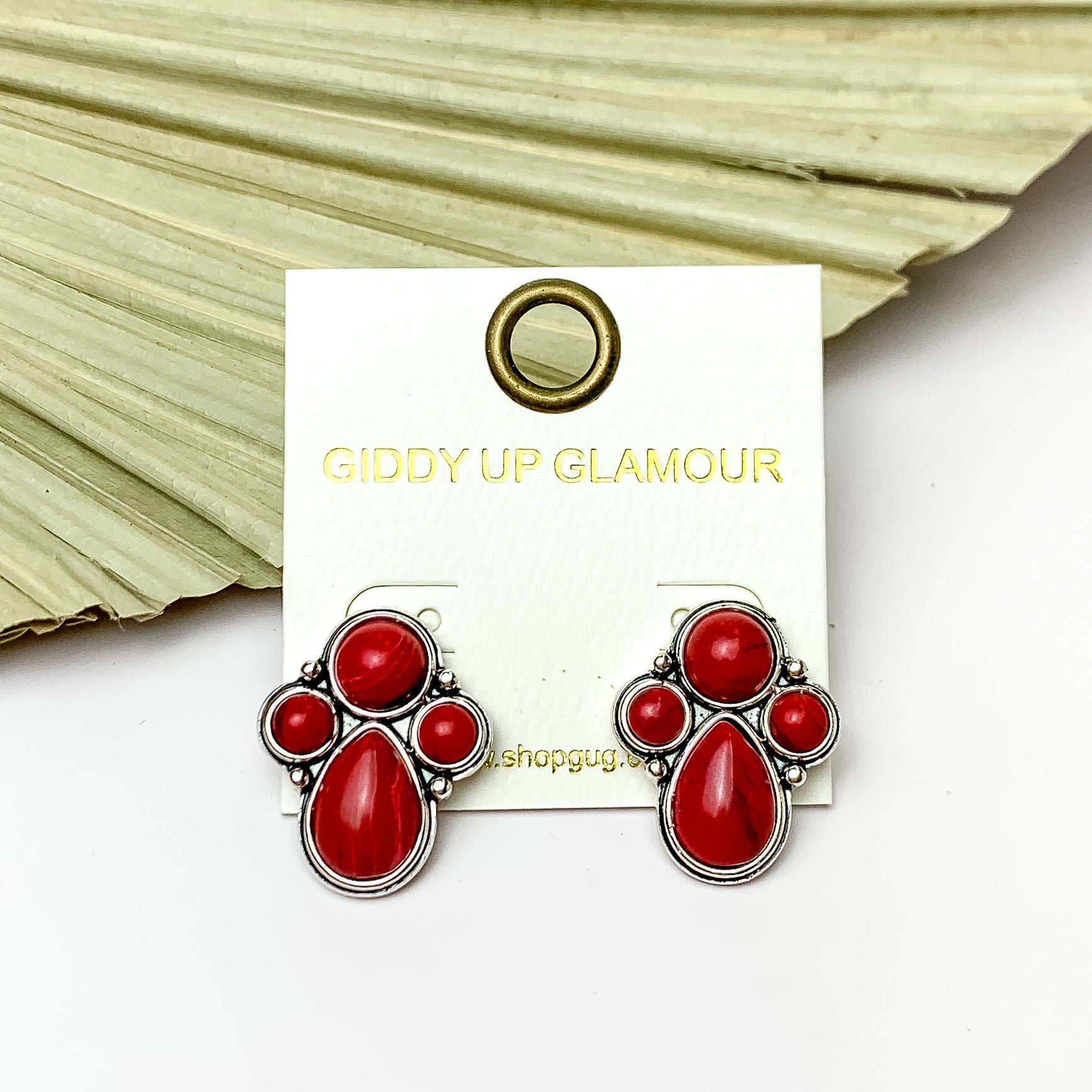 Silver Tone Cluster Stone Earrings in Red. Pictured on a white background with a leaf fan behind the earrings.