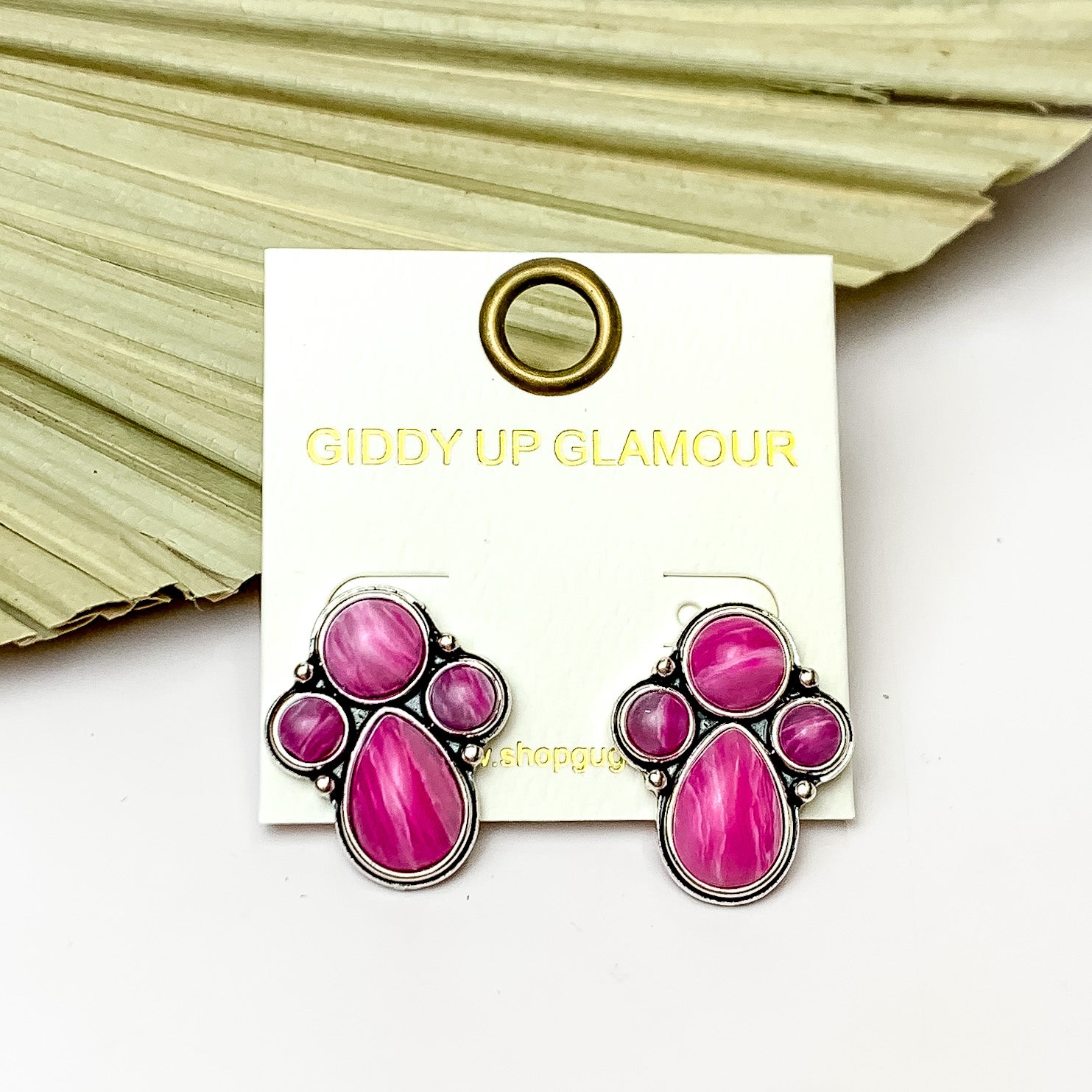 Silver Tone Cluster Stone Earrings in Light Pink. Pictured on a white background with a fan leaf behind the earrings.