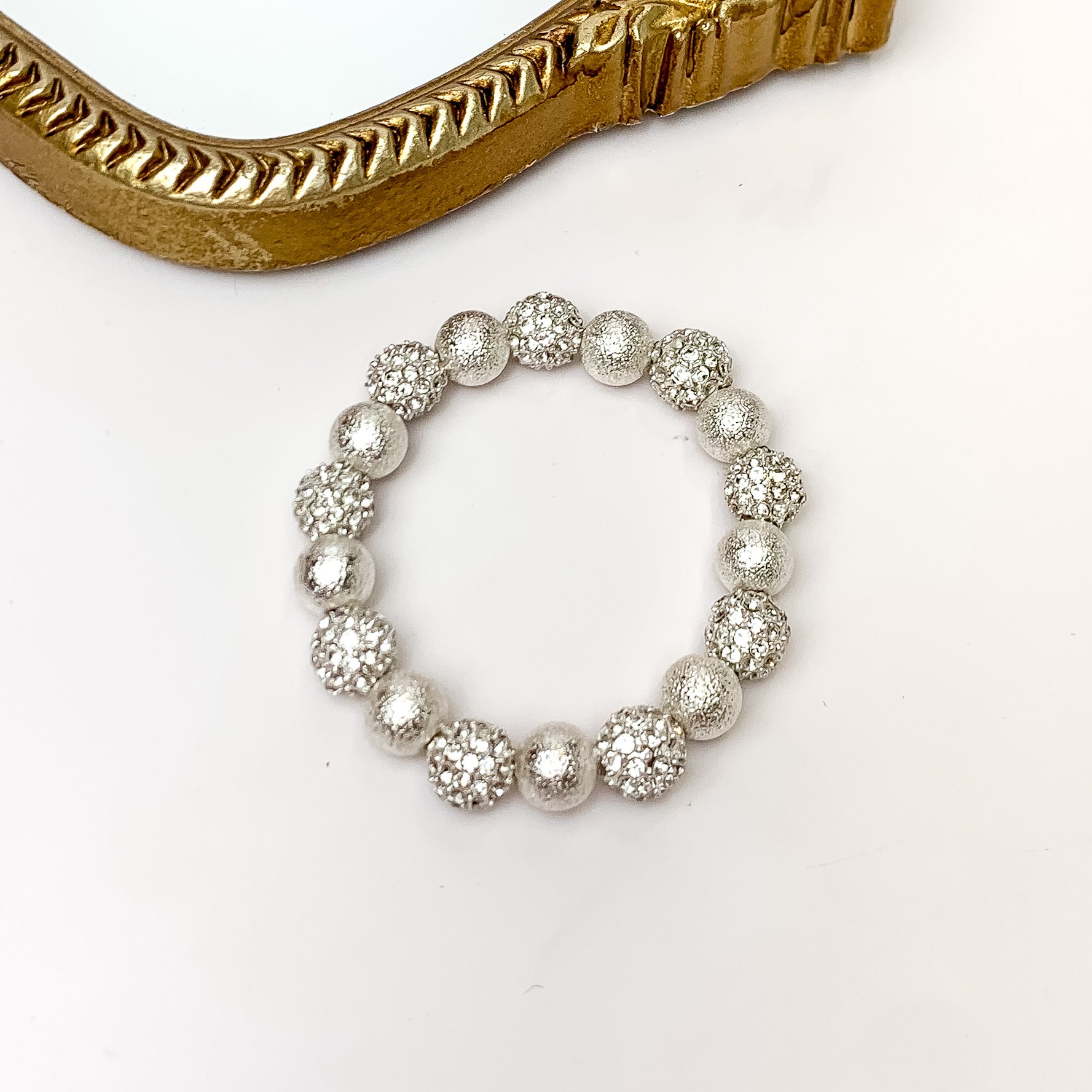 Clear crystal and silver beaded bracelet pictured on a white background with a gold mirror in the top left corner. 