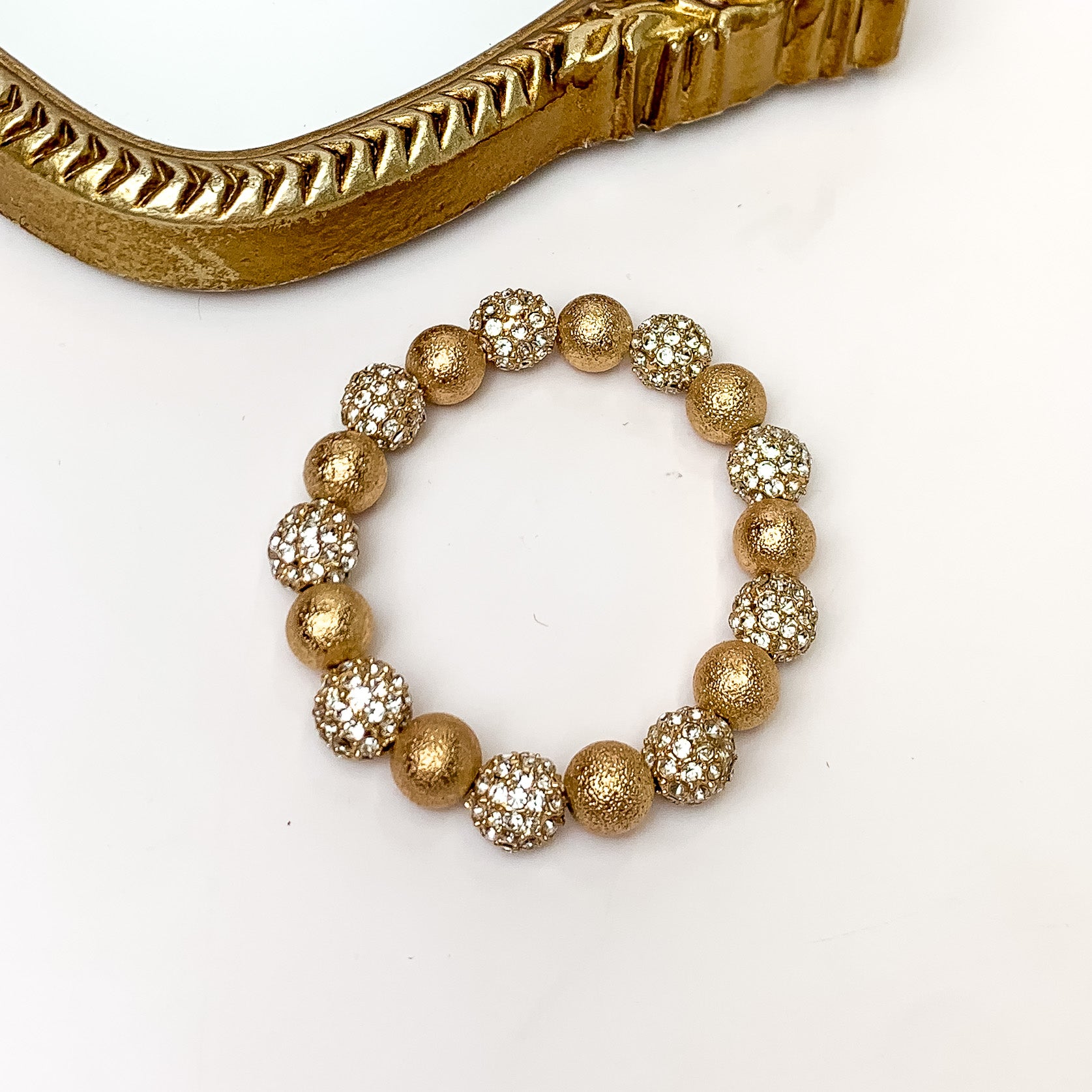 Clear crystal and gold beaded bracelet pictured on a white background with a gold mirror in the top left corner. 