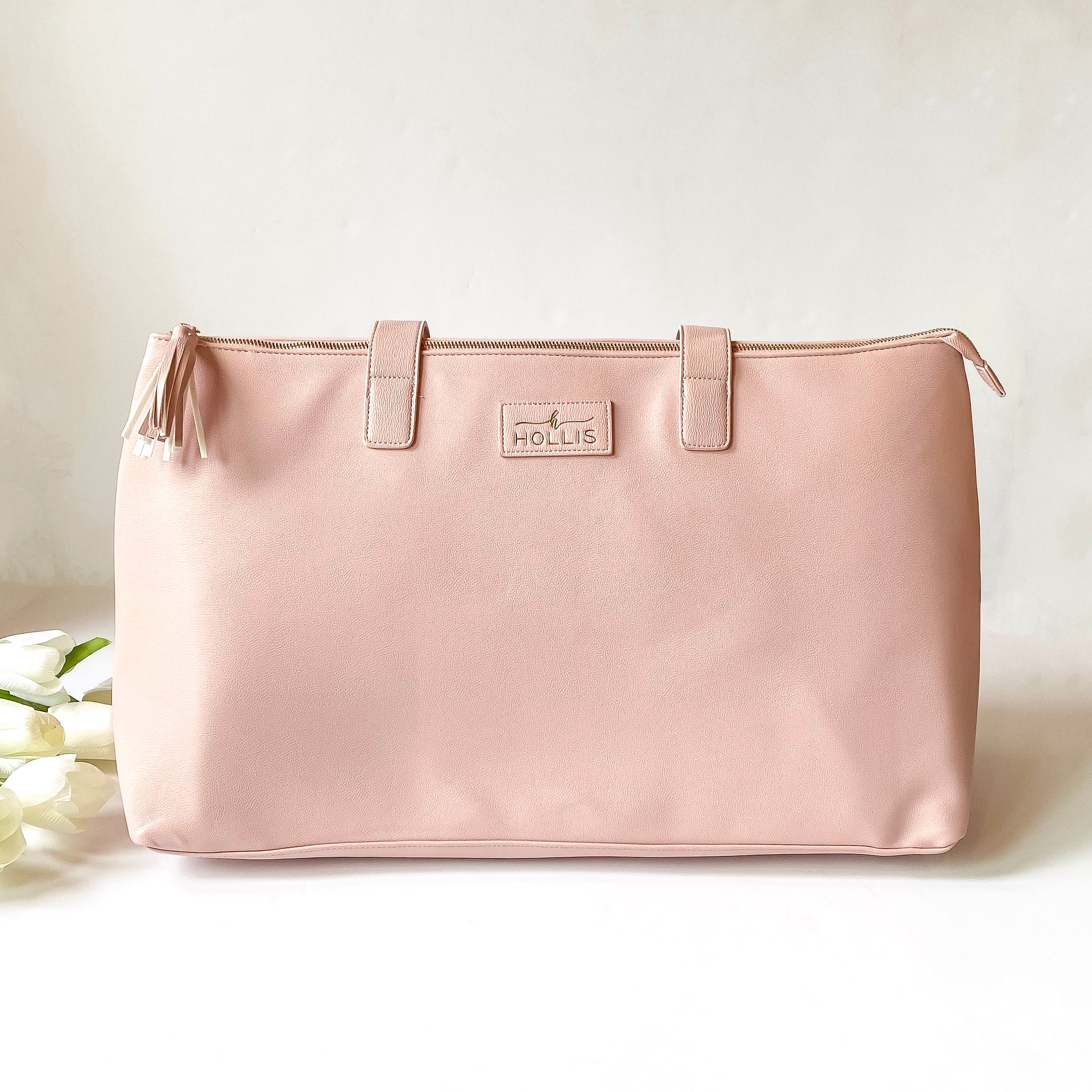 Blush pink duffle bag with a top zipper and blush pink handles. This bag is pictured on a white background with white flowers on the left side of the bag.