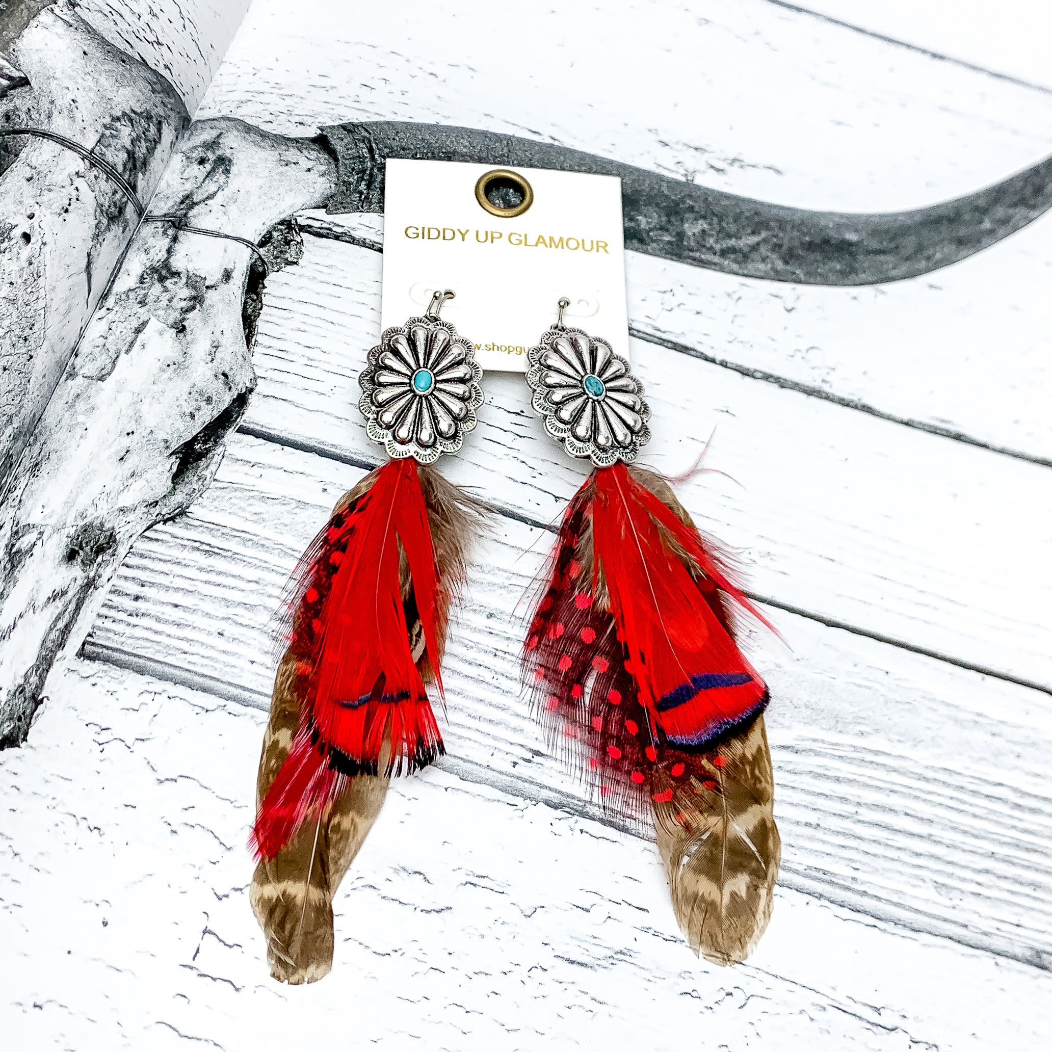 Desert Doll Silver Tone Feather Earrings in Red. Pictured on a western page with a longhorn on the page.