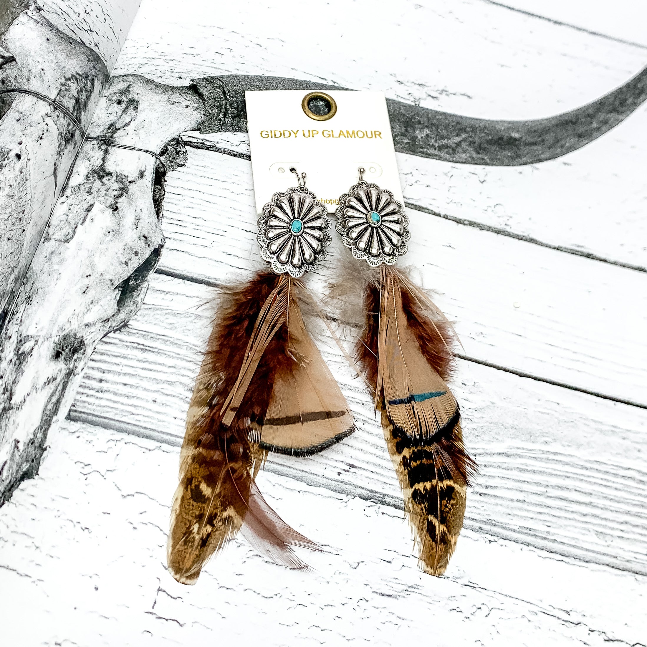 Desert Doll Silver Tone Feather Earrings in Brown. Pictured on a page of a western book.