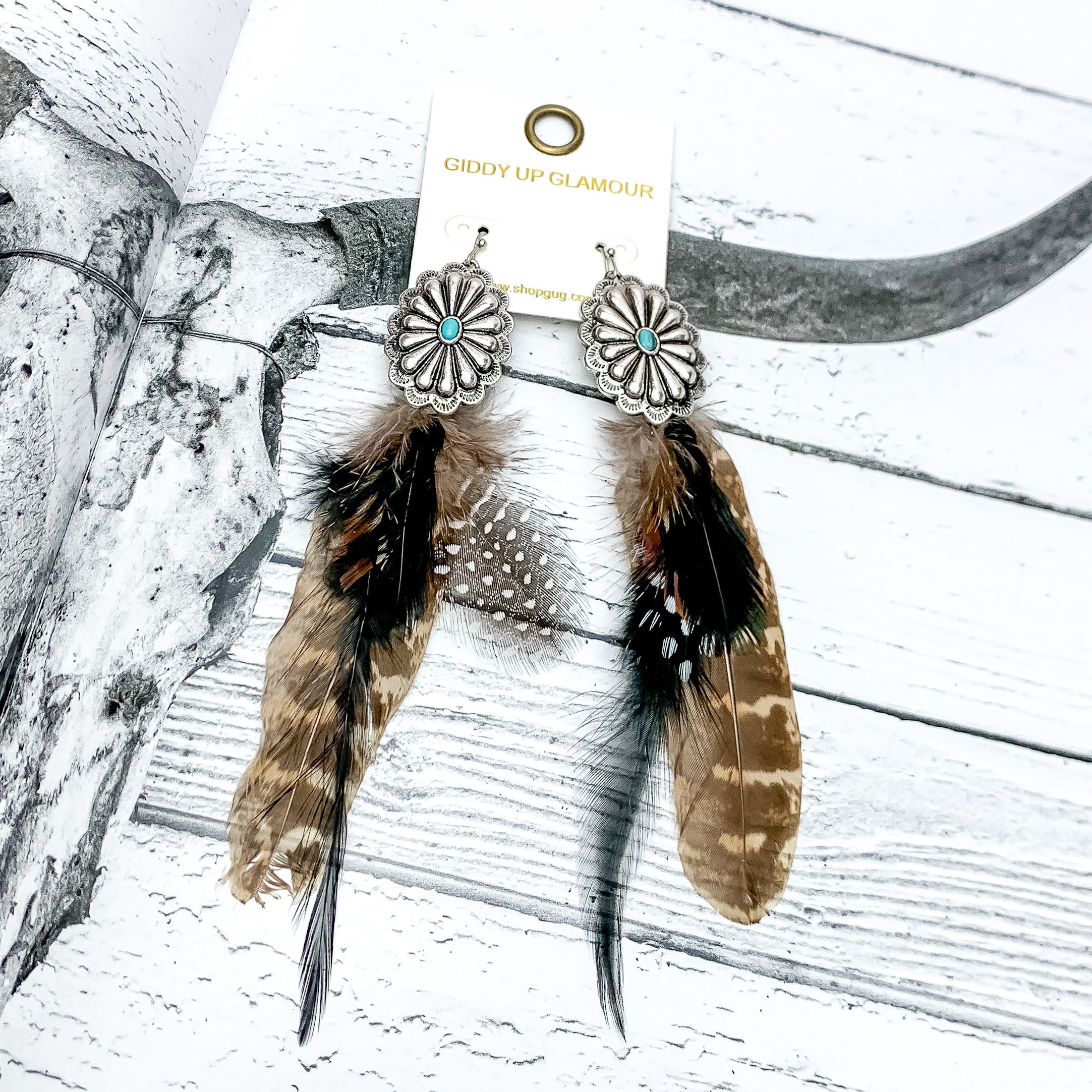 Desert Doll Silver Tone Feather Earrings in Black. Pictured on an open book with a western picture.
