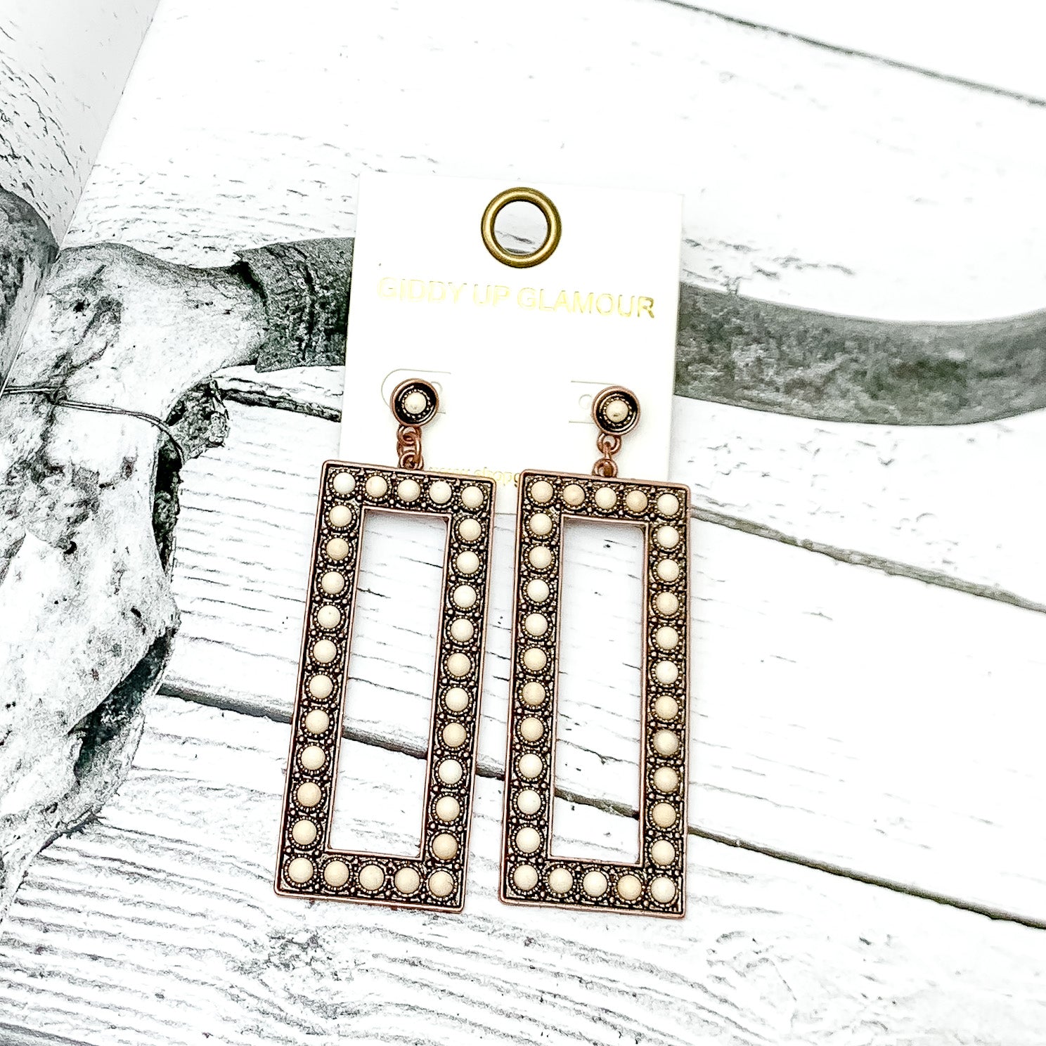 Copper Tone Rectangular Drop Earrings With Stones in Ivory. Pictured on an open page with a western background.