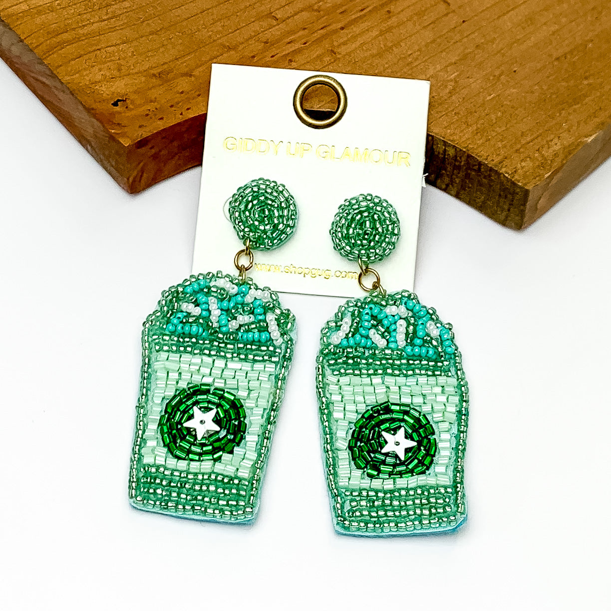 Coffee with The Whip Beaded Earrings in Mint Green. Pictured on a white background laying against a piece of wood. 