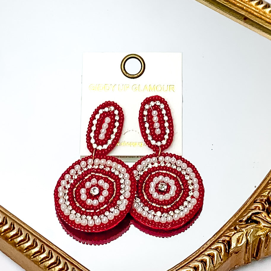 Maroon Circle Earrings With Clear Crystals and Pearls. Pictured on a mirror with a gold frame around it.