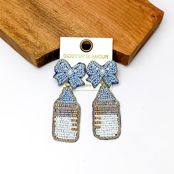 Baby Blue and White Beaded Bottle Earrings with Blue Bow Studs. Pictured on a white background with the earrings leaning against a piece of wood.